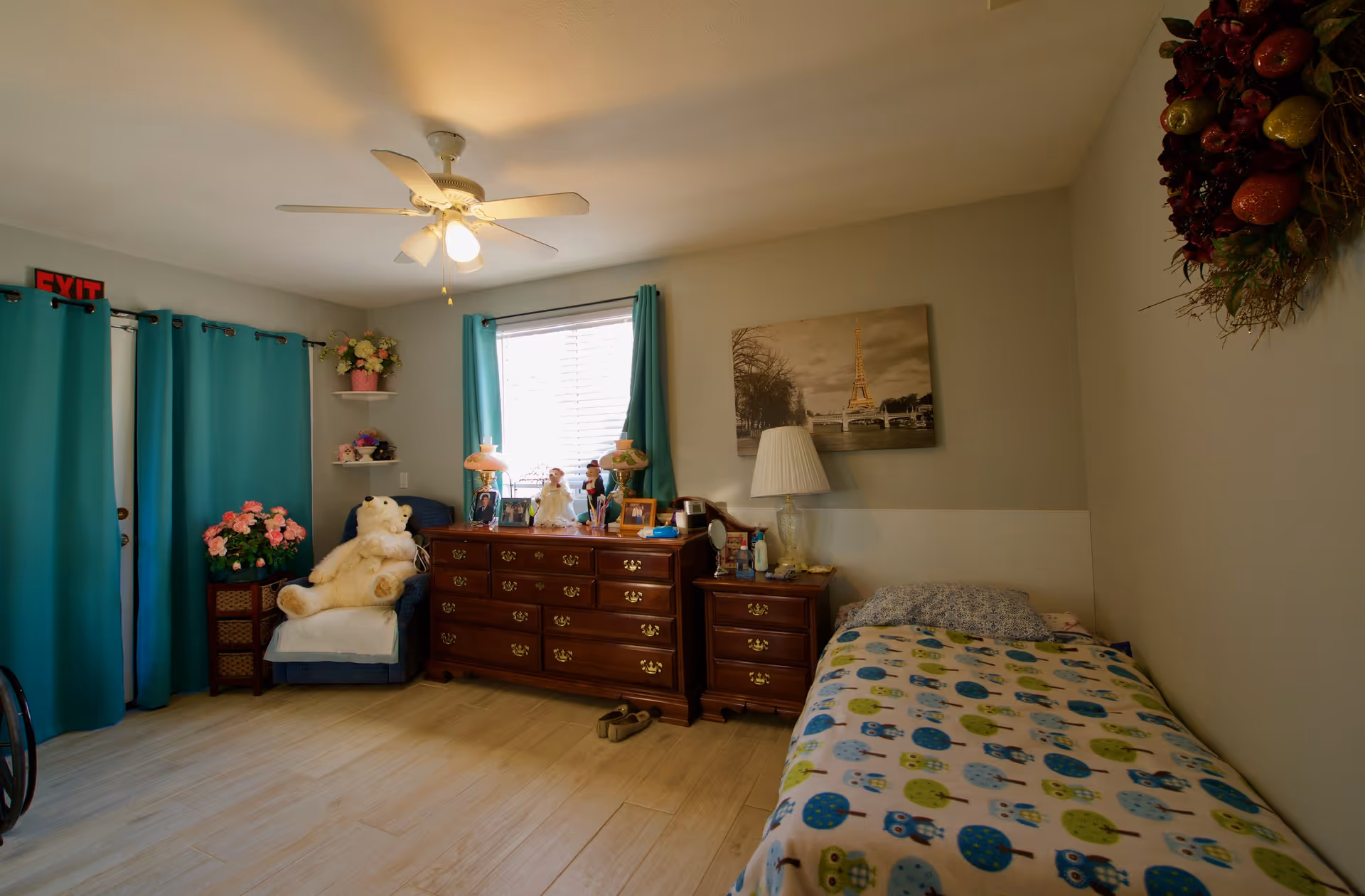 Cozy bedroom featuring a single bed, dresser, turquoise curtains, and decorative items.