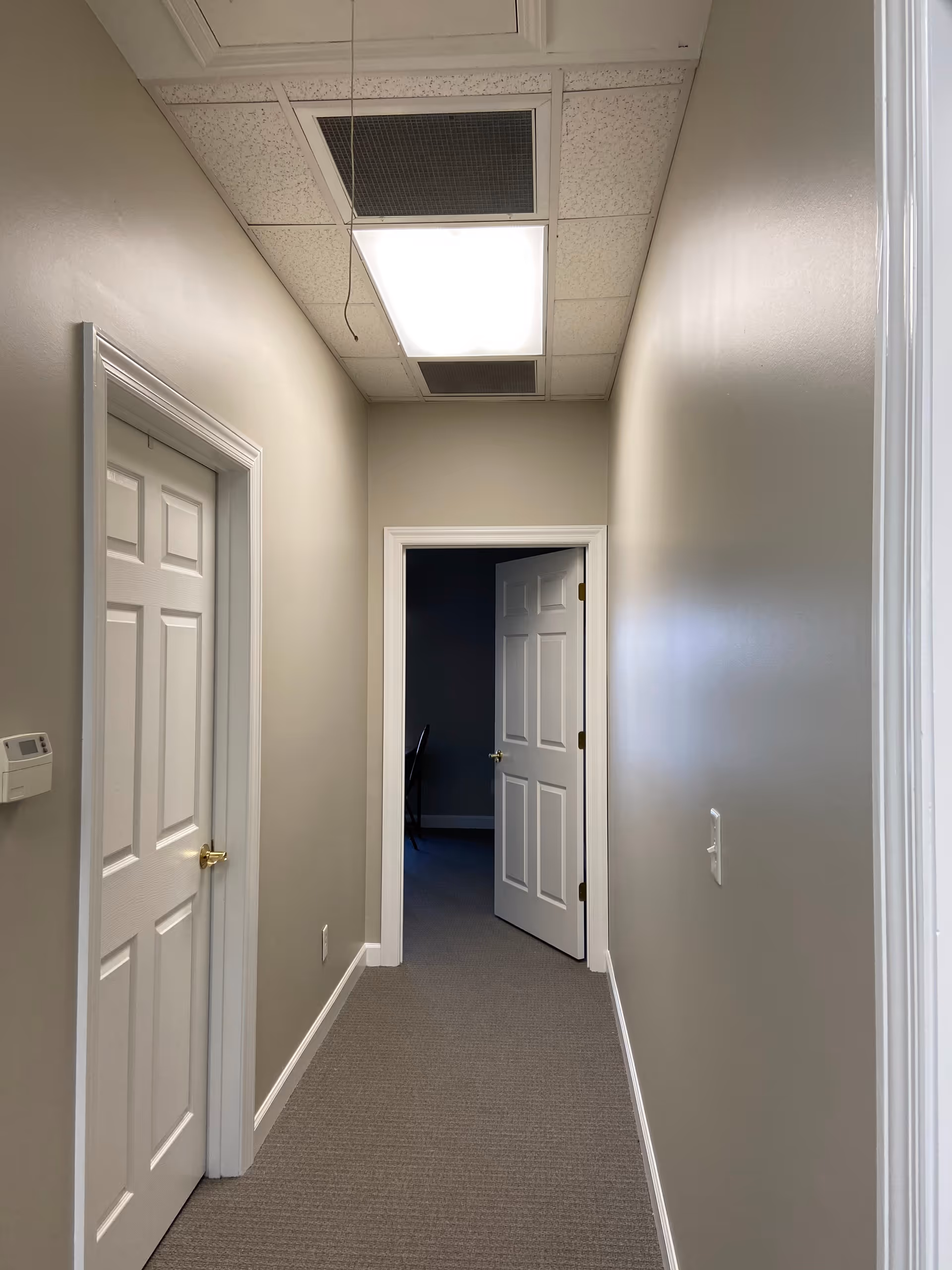 Empty beige hallway with closed doors, carpet, and bright fluorescent ceiling lights.