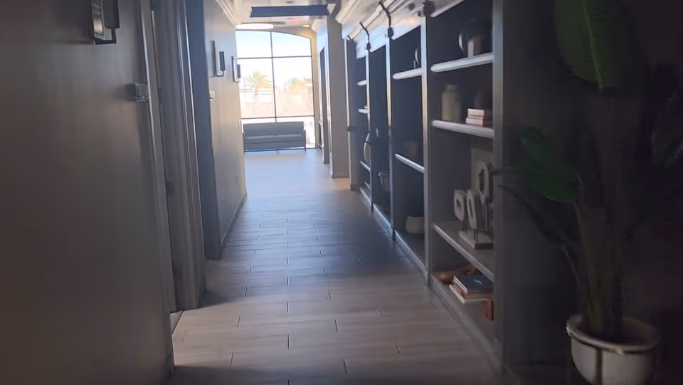 Long, well-lit interior hallway with shelves on the right and a seating area at the end.