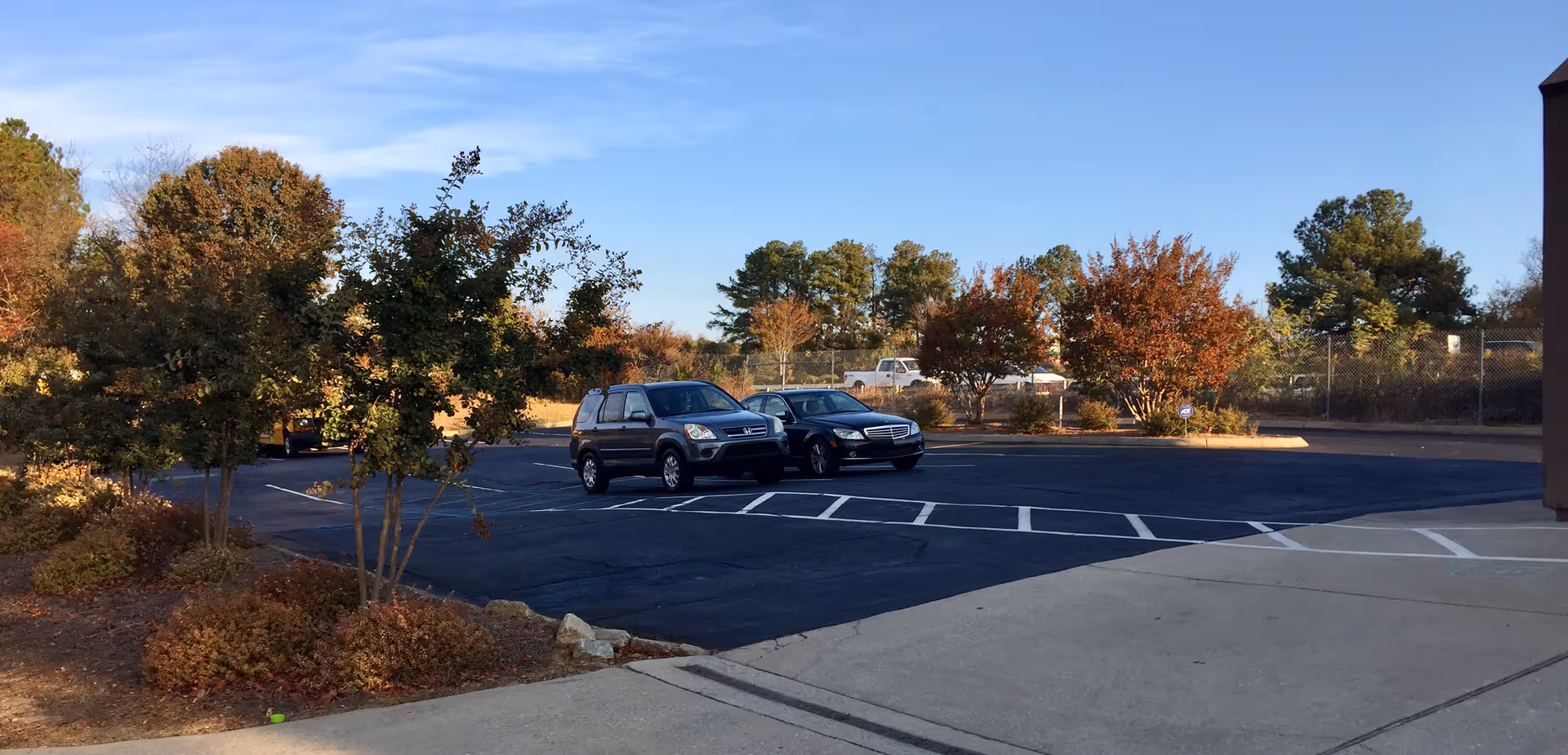 Sunny parking lot with parked cars and trees near a facility