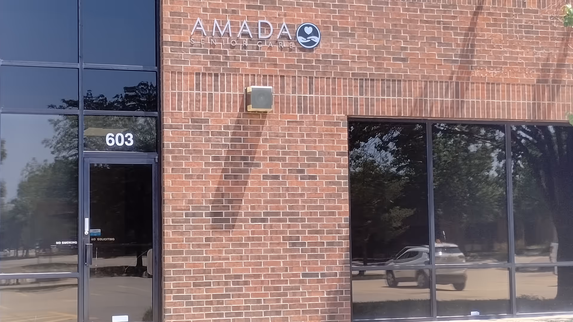 Brick building facade with Amada Senior Care sign and large front windows.