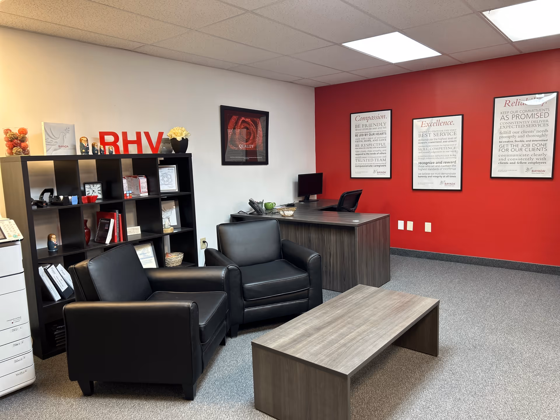 Reception area with black leather chairs, desk, red wall, and BAYADA branding.