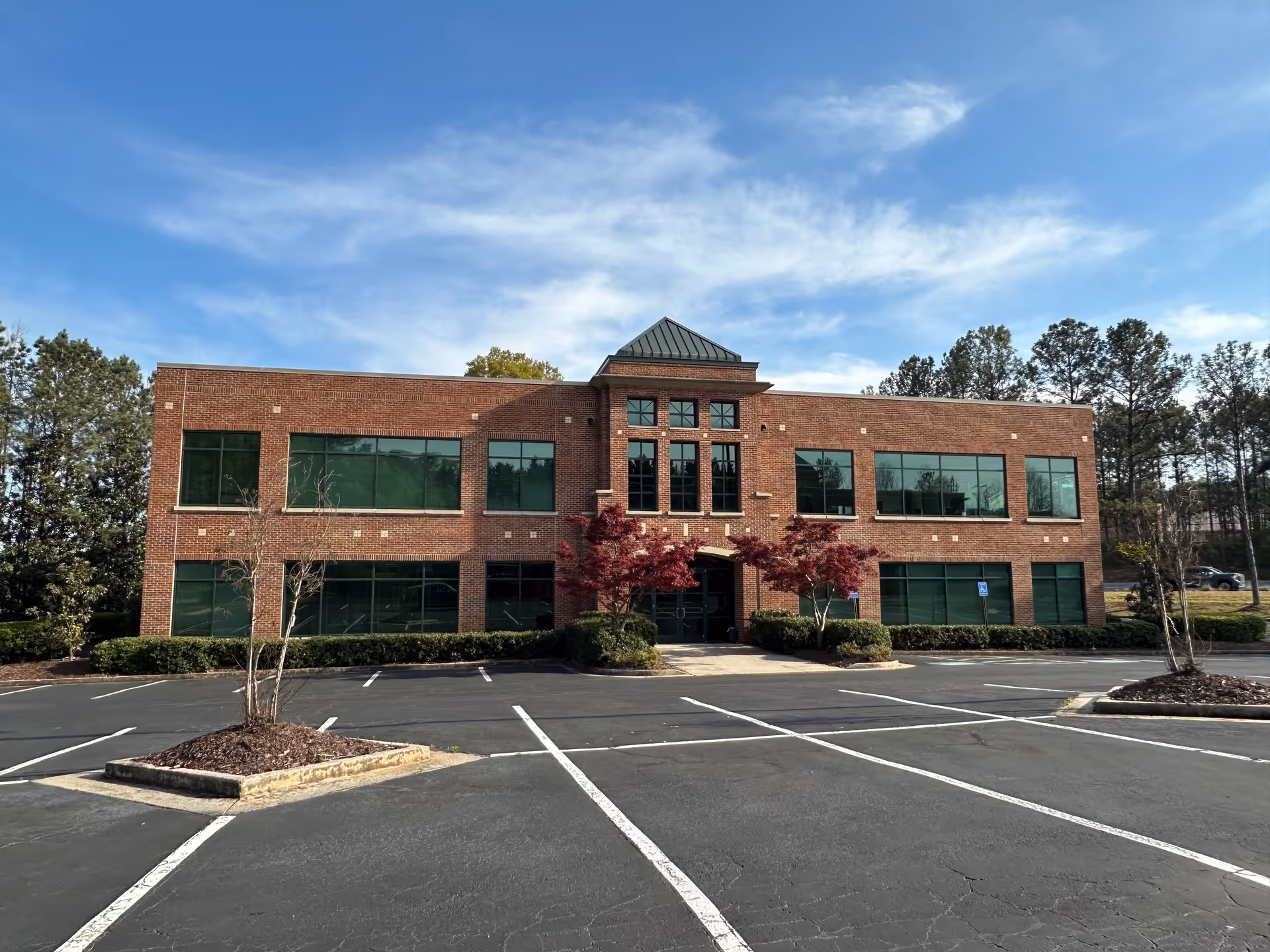 Brick senior living facility building with large windows and a parking lot in front.