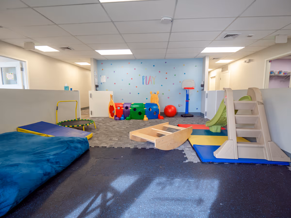 Indoor activity room with play equipment, soft mats, and a small slide.