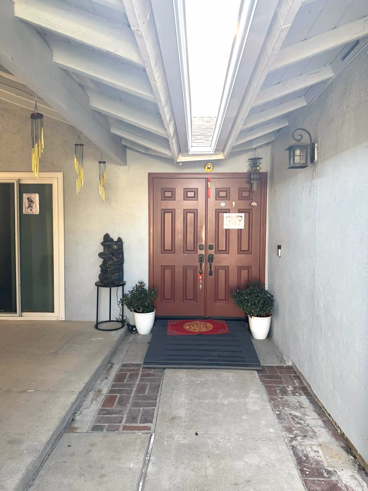 Double wooden doors at a covered entrance with potted plants and a welcome mat.