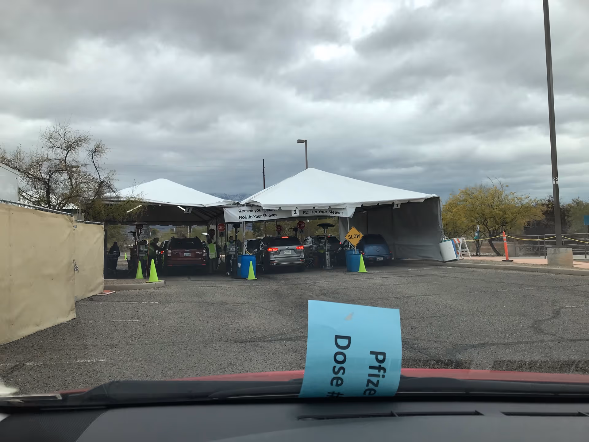 Drive-through health screening tents outside a facility with cars and staff assisting