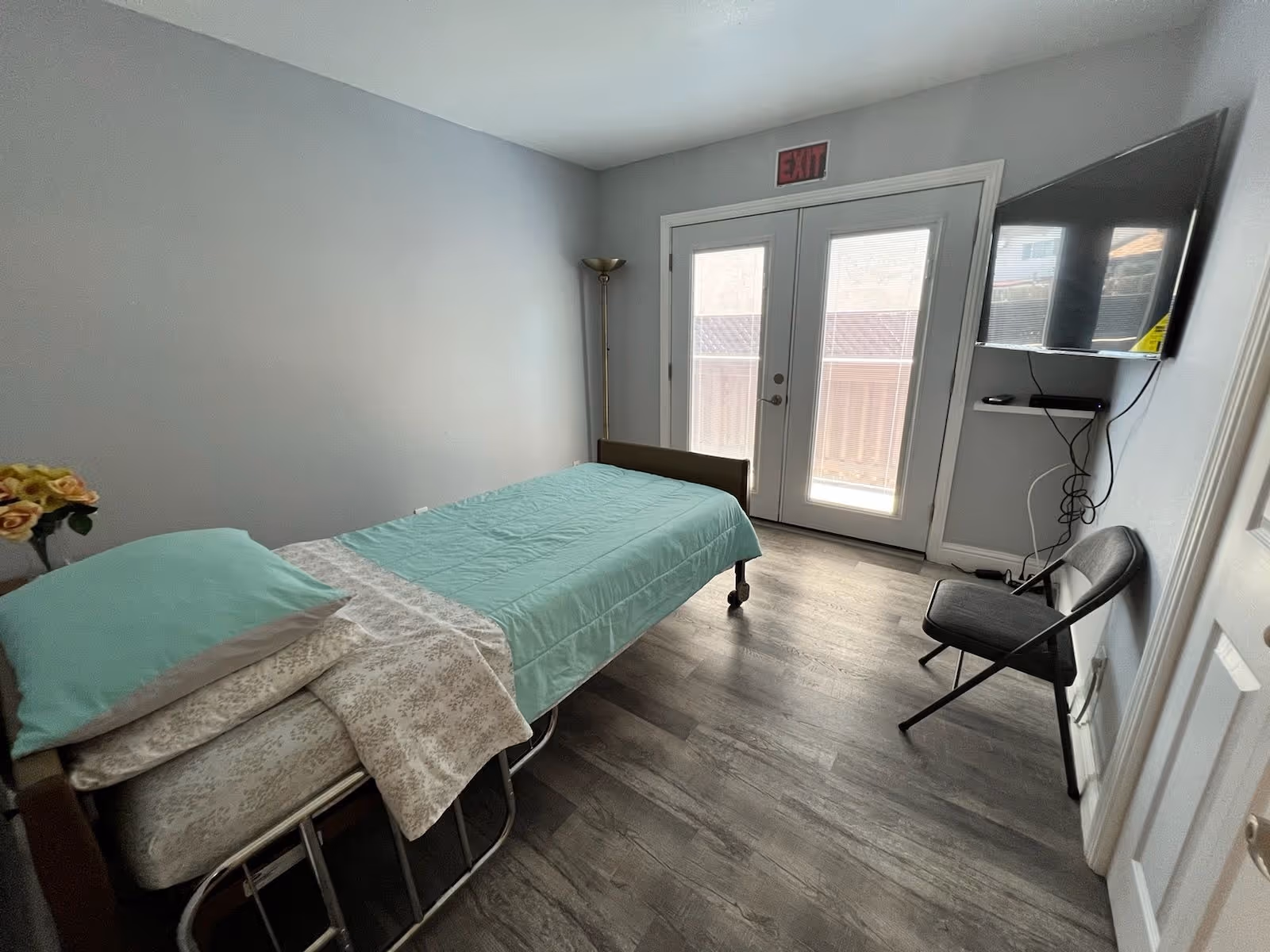 A small bedroom in a senior living facility with a bed, TV, and chair.