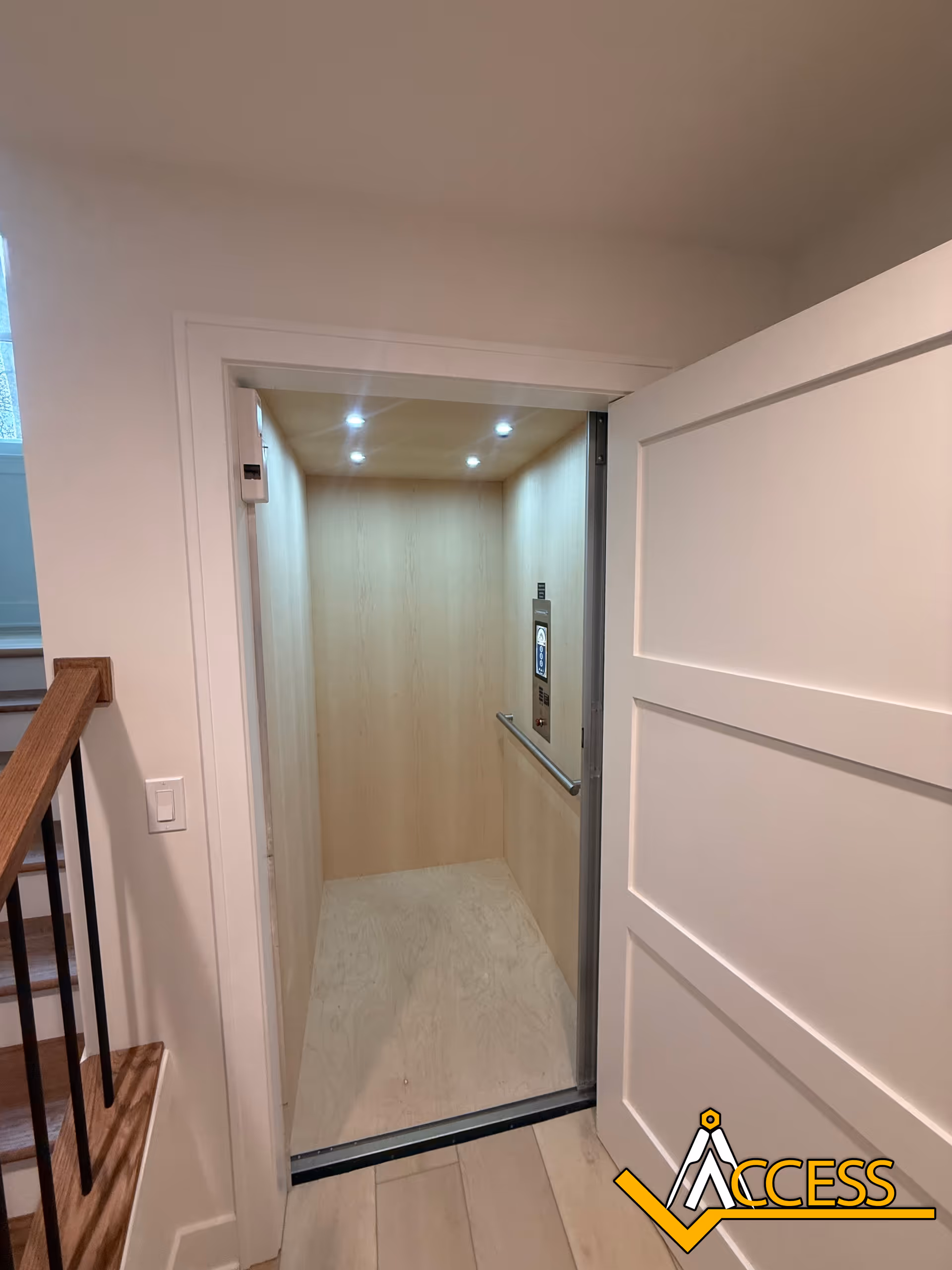 Interior elevator with light wood panels and a nearby stair railing