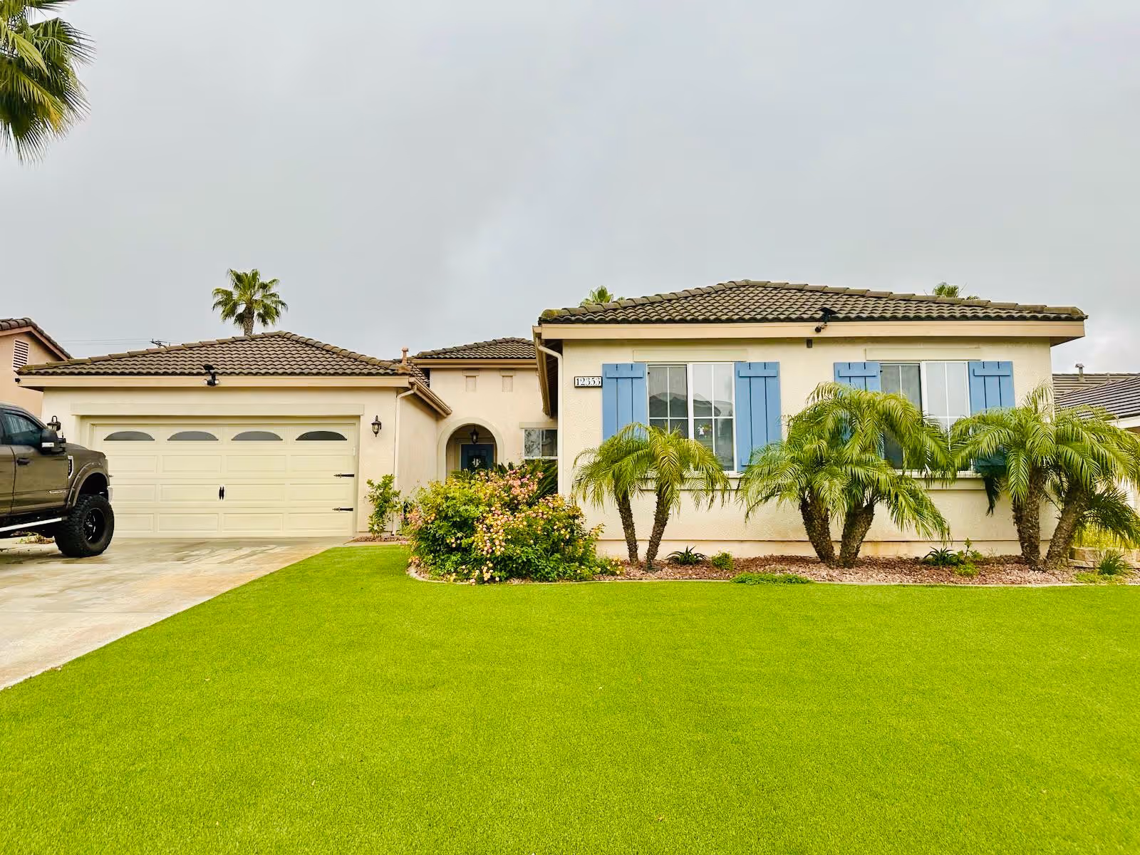 Single-story house with two-car garage, manicured lawn, and palm trees in front yard