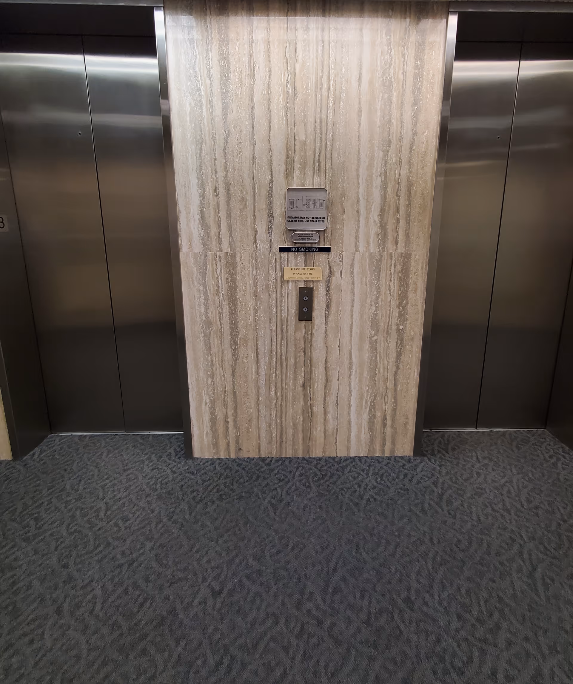 Interior elevator hallway with two doors and central stone wall panel.