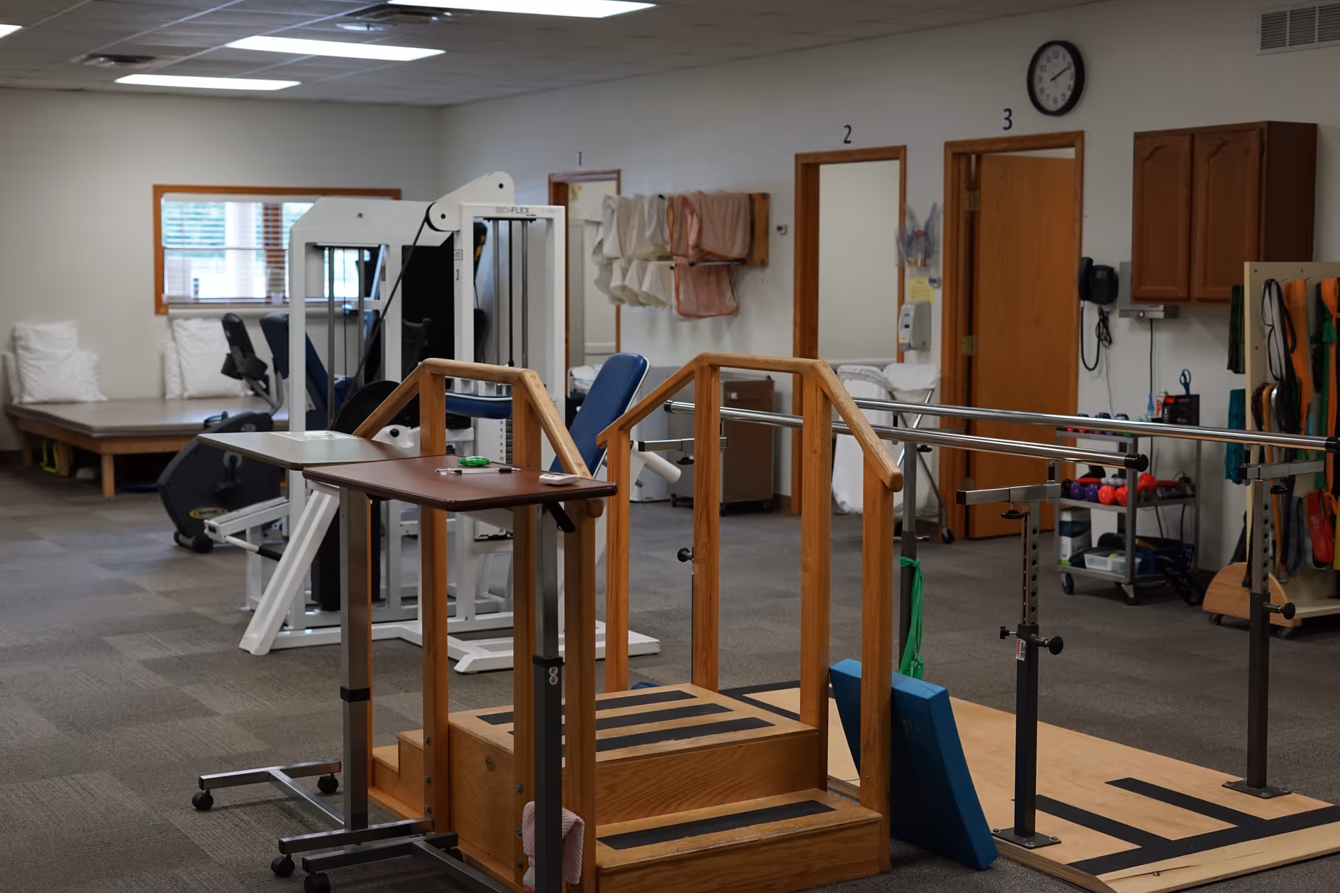 Interior physical therapy room with parallel bars, gym equipment, and benches.