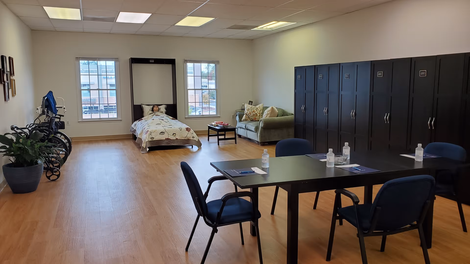Spacious senior living room with a bed, couch, dining table, and lockers.