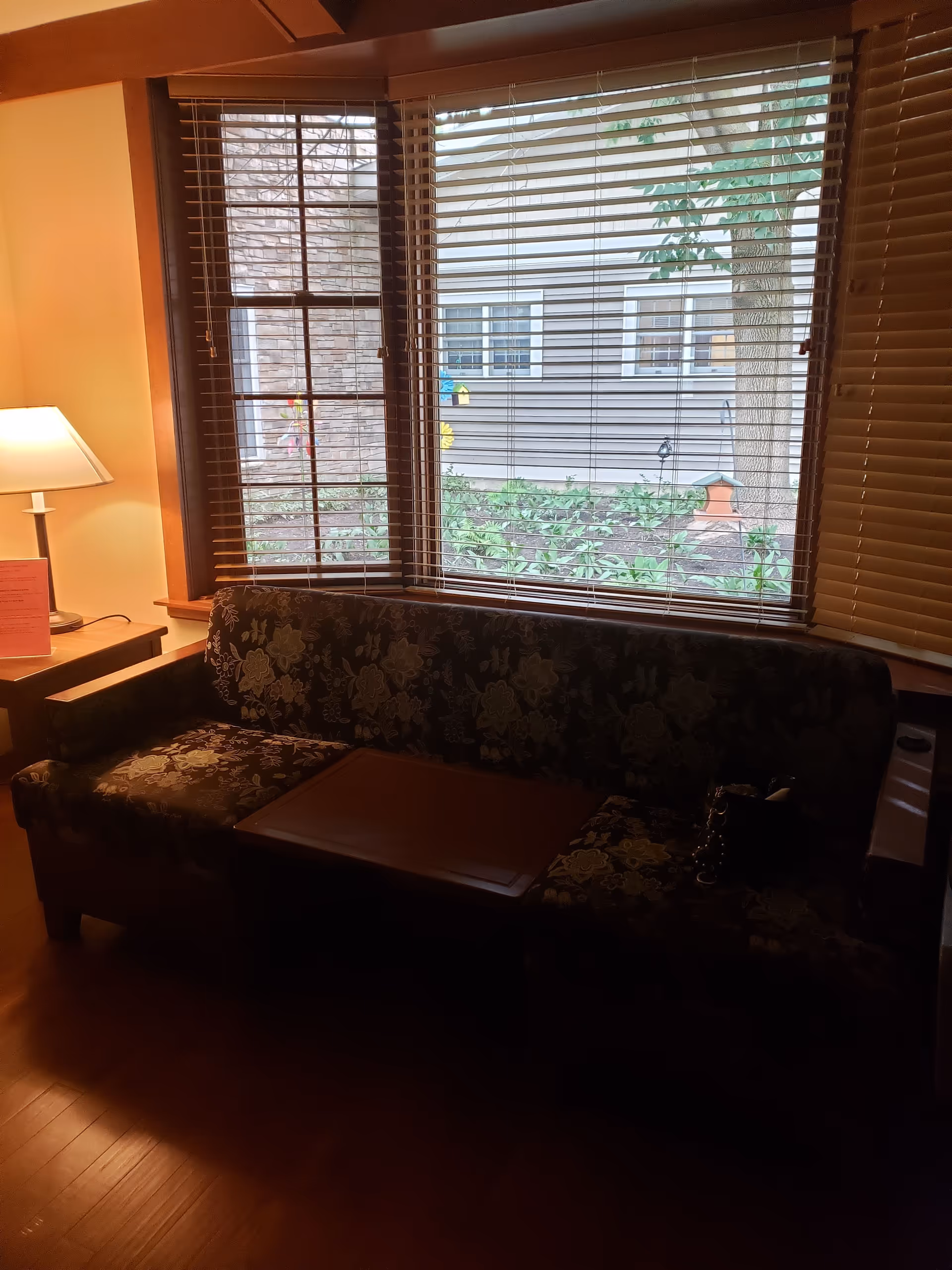 Cozy living room with floral-patterned sofa, wooden coffee table, lamp, and window blinds.