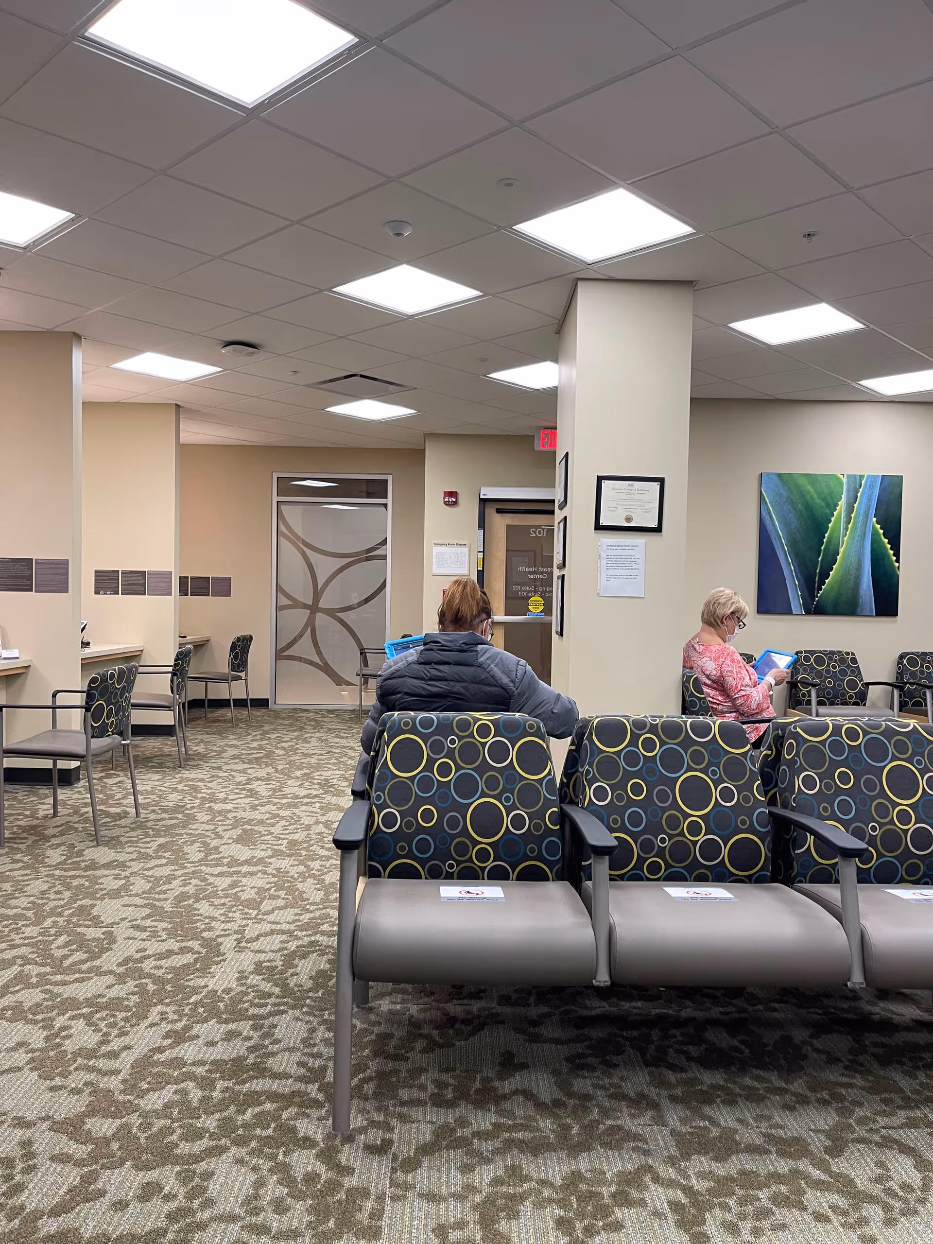 Interior waiting area at Norton Healthcare Medical Plaza III Brownsboro with patterned chairs and two visitors.