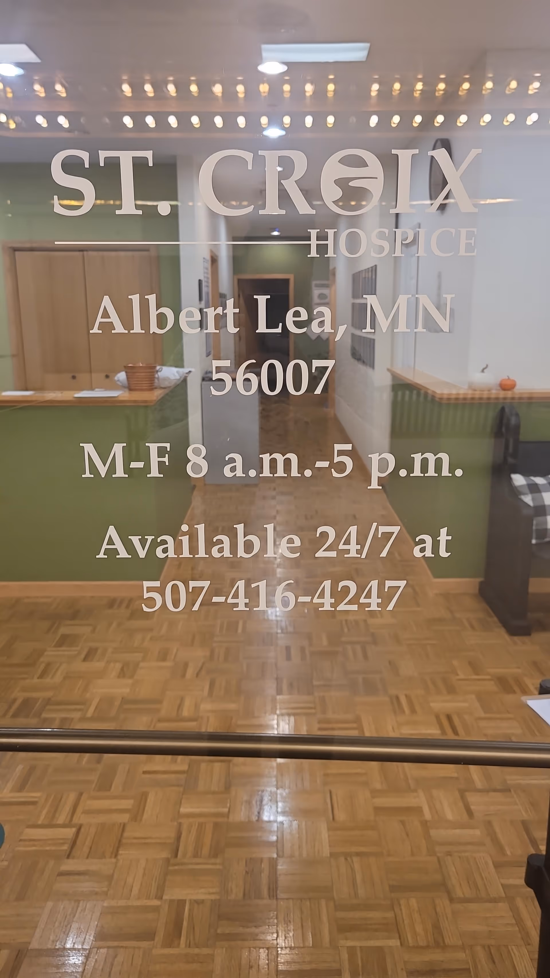 Glass door with St. Croix Hospice text reveals interior lobby with green counters and wooden floor.