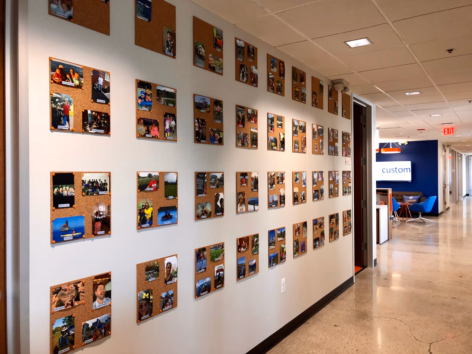 Hallway with photo corkboards along white wall, leads to blue seating area in senior facility.