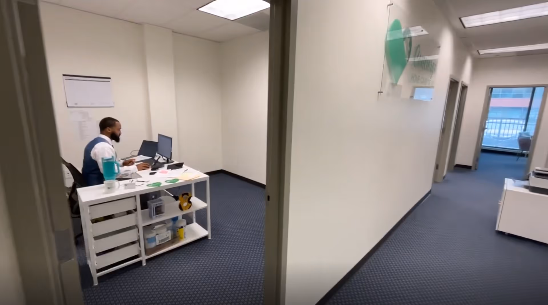 Staff member working at a white desk in a hallway office of a senior care facility.