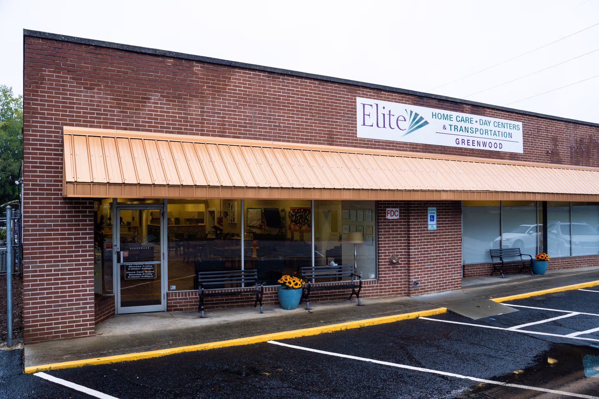 Exterior view of a brick Elite Home Care Day Centers building with orange canopy and benches.