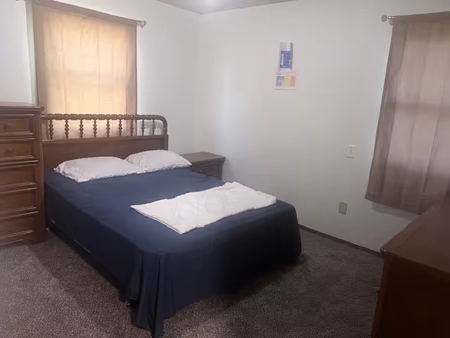 A tidy bedroom with a dark wood bed, dresser, two nightstands, and curtained windows.