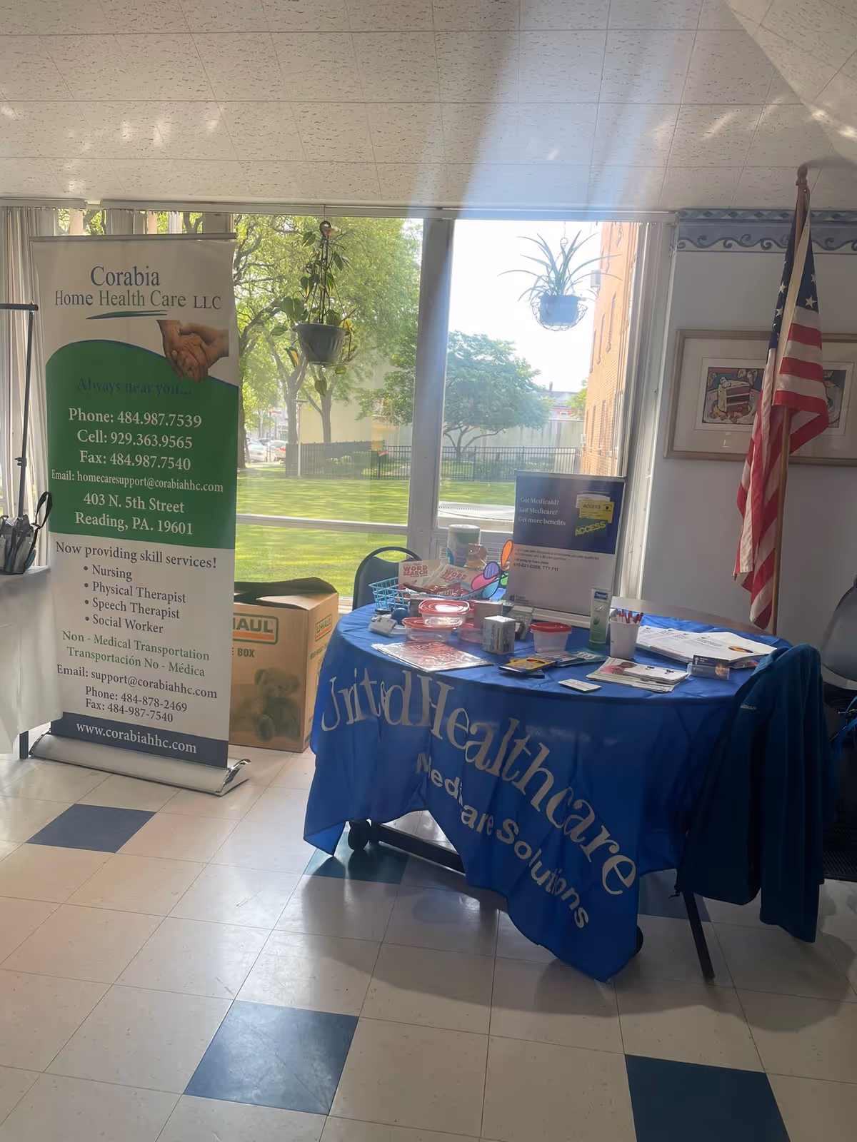 Indoor lobby with Corabia Home Health Care banner and blue-cloth table display near windows.