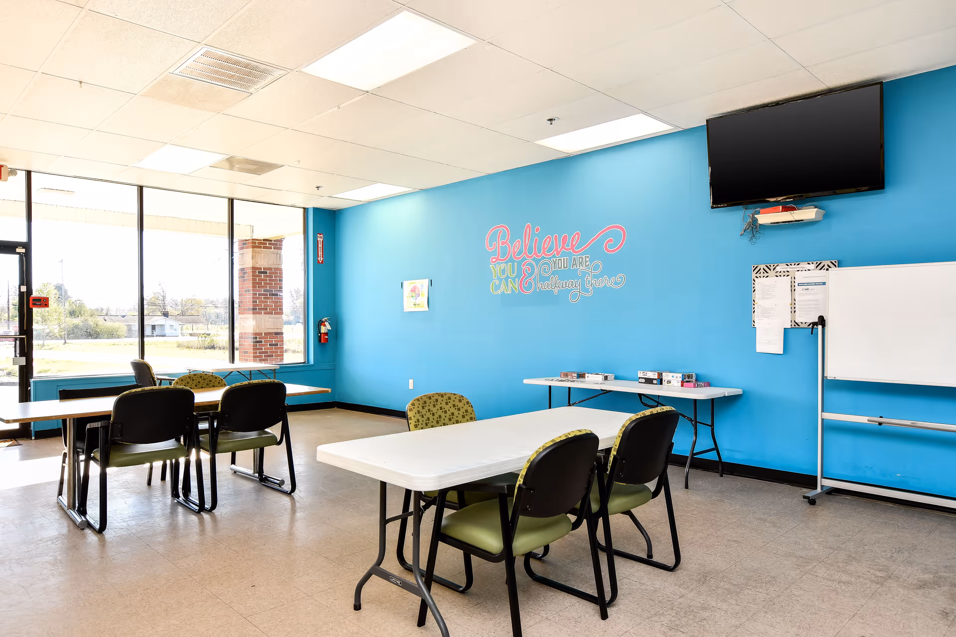 Bright blue-walled activity room at a senior facility with tables, chairs, and whiteboard.