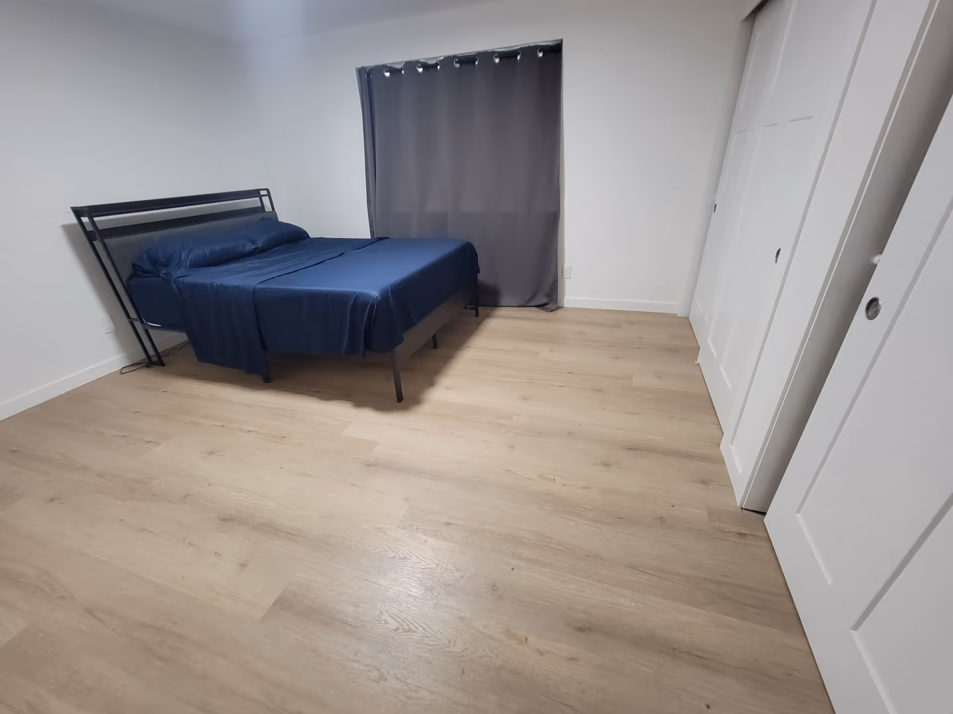 Bedroom with a blue bed, gray curtains, white walls, and closet doors.