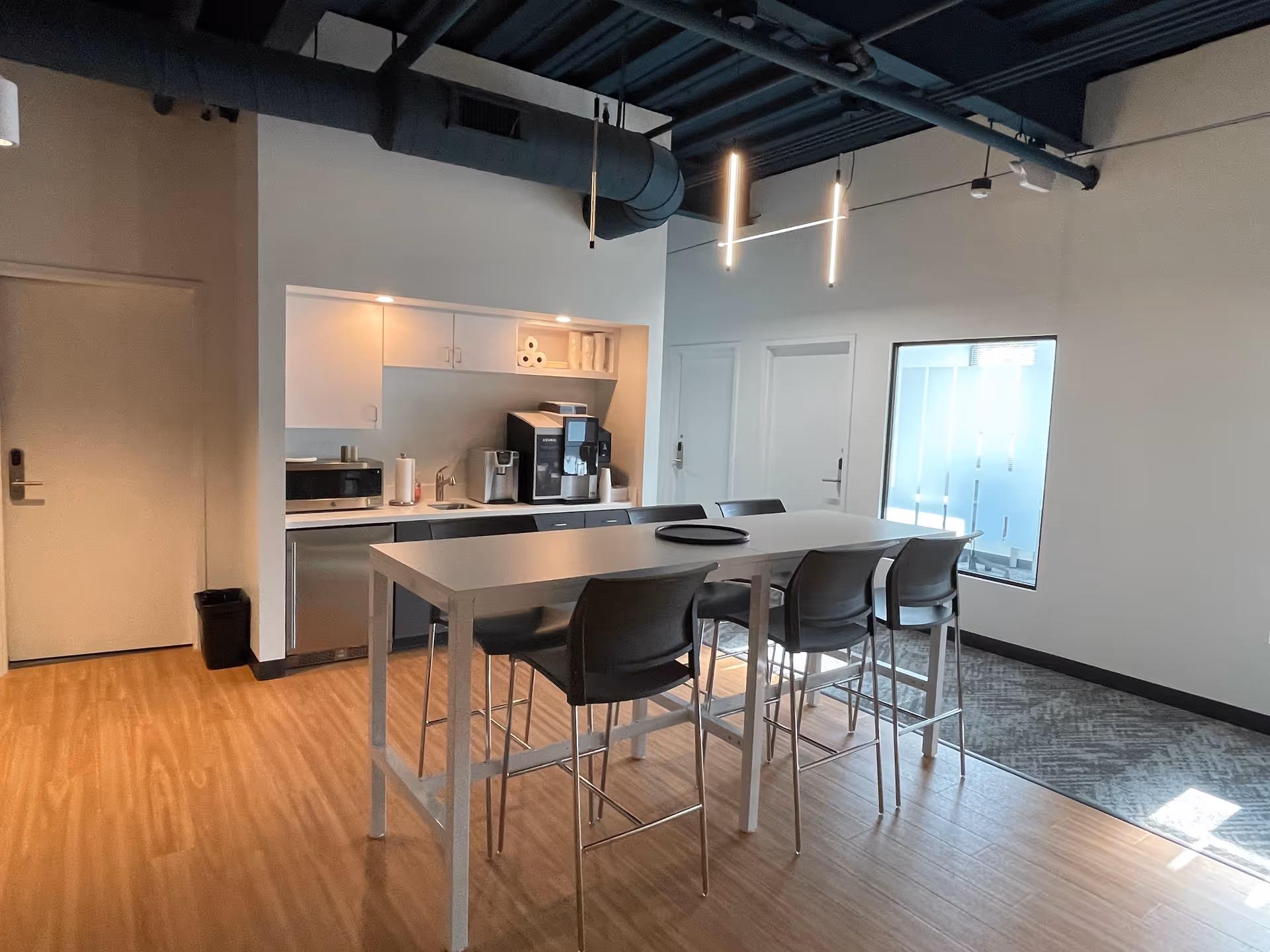 Interior common area with a white kitchenette, high table, and bar-stool seating.