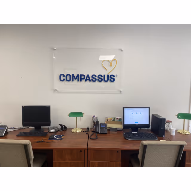 Front desk workspace with two computers and a Compassus sign on the wall.