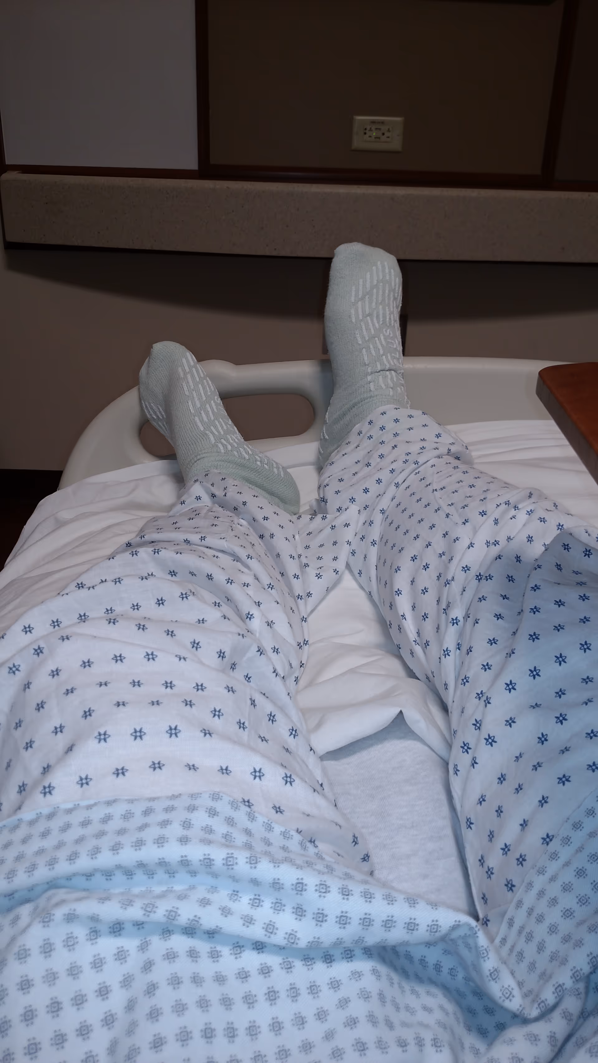View from patient’s bed showing legs in a hospital gown and socks.