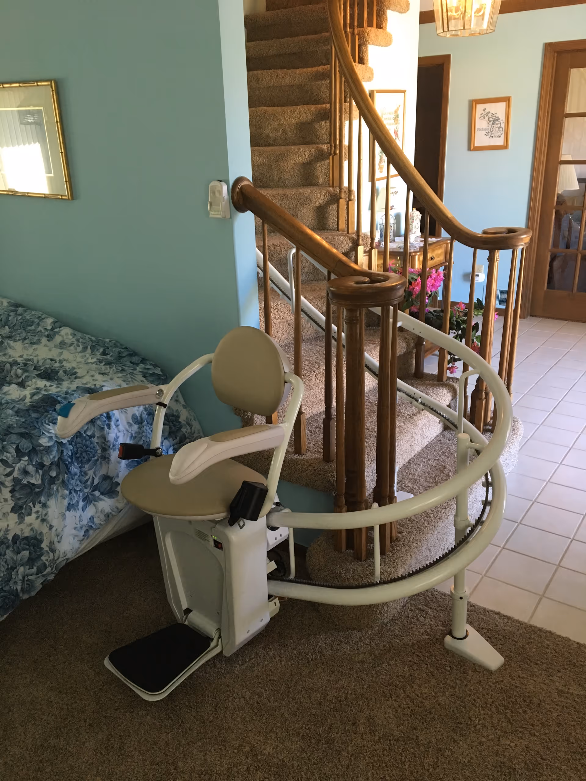 A mobility patient lift beside a bed in a bedroom near a curved staircase.