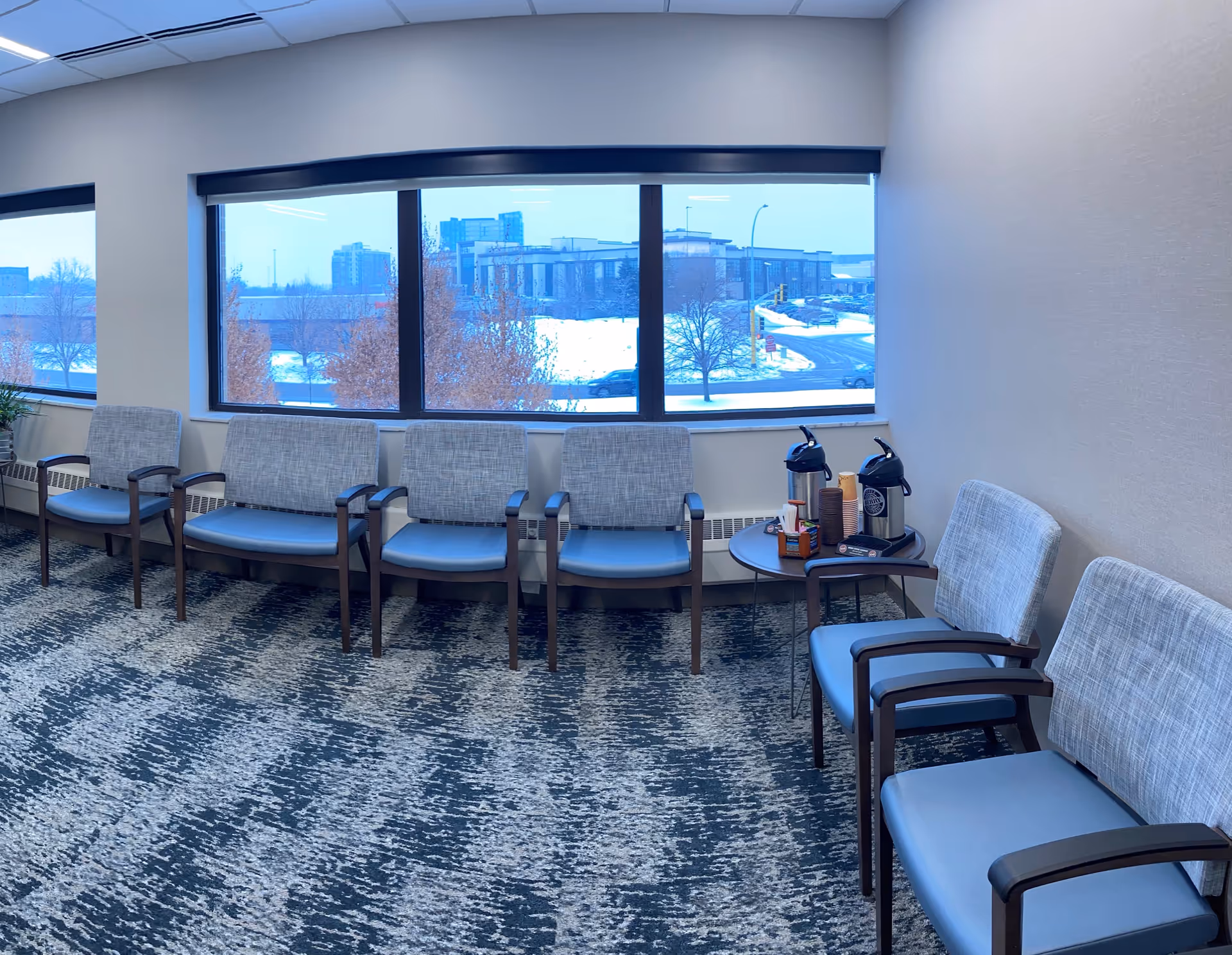 Row of blue chairs along a large window in a waiting lounge.