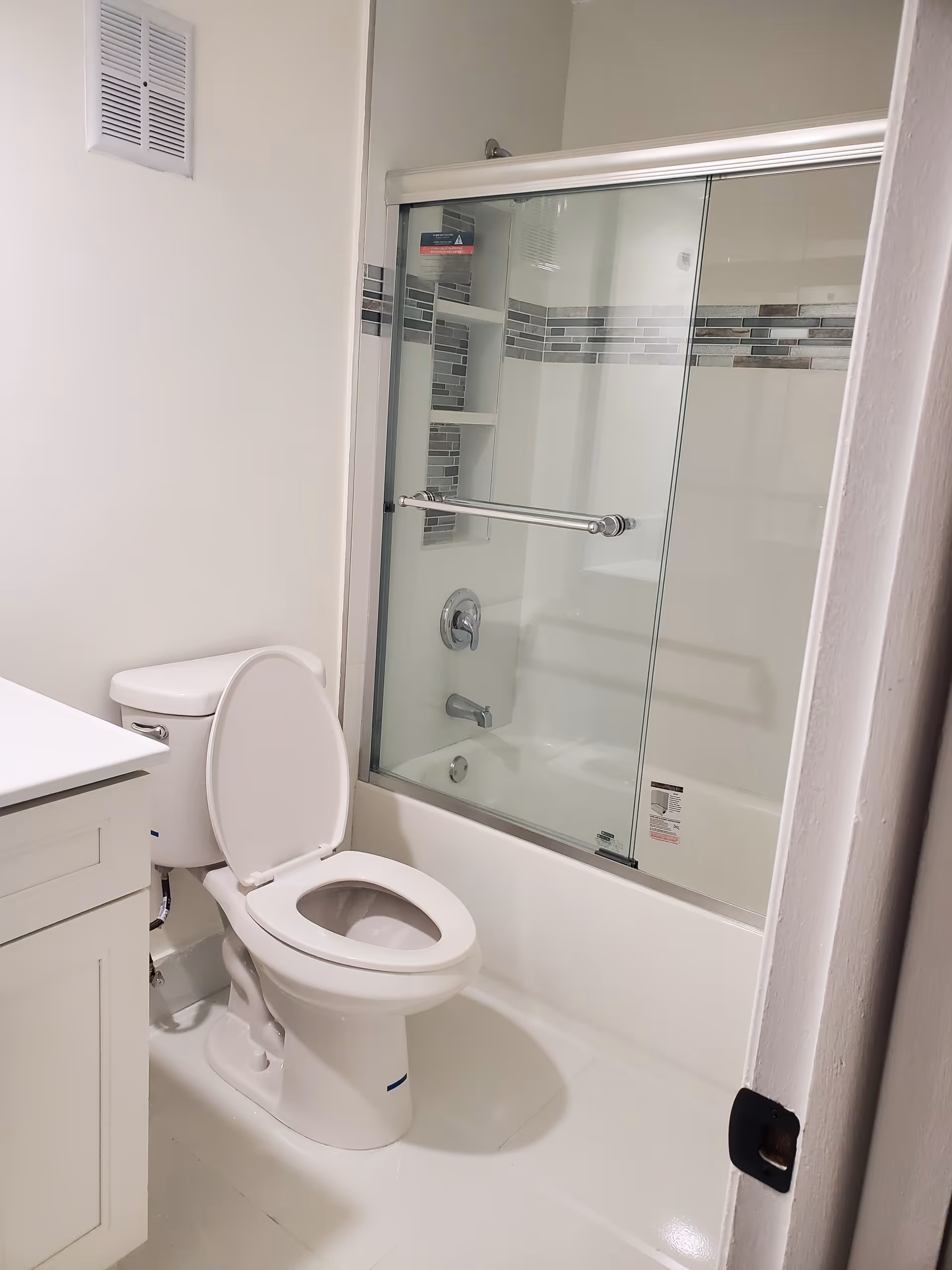 White bathroom with toilet, vanity, and glass shower enclosure.