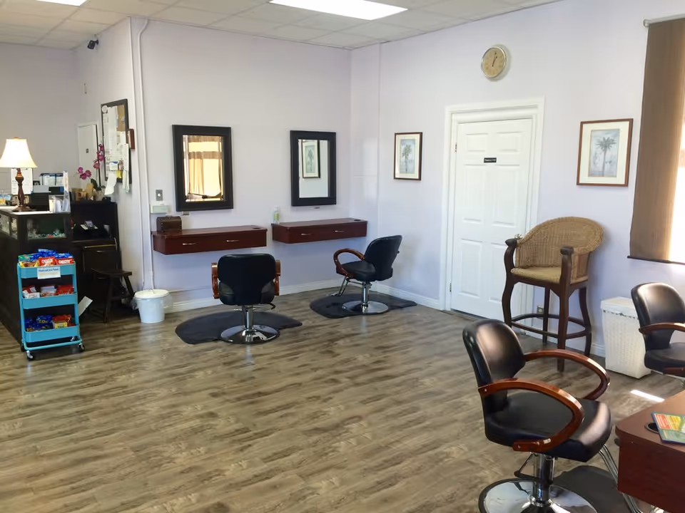 A salon area with hair styling chairs, mirrors, and cart of supplies in a bright room.