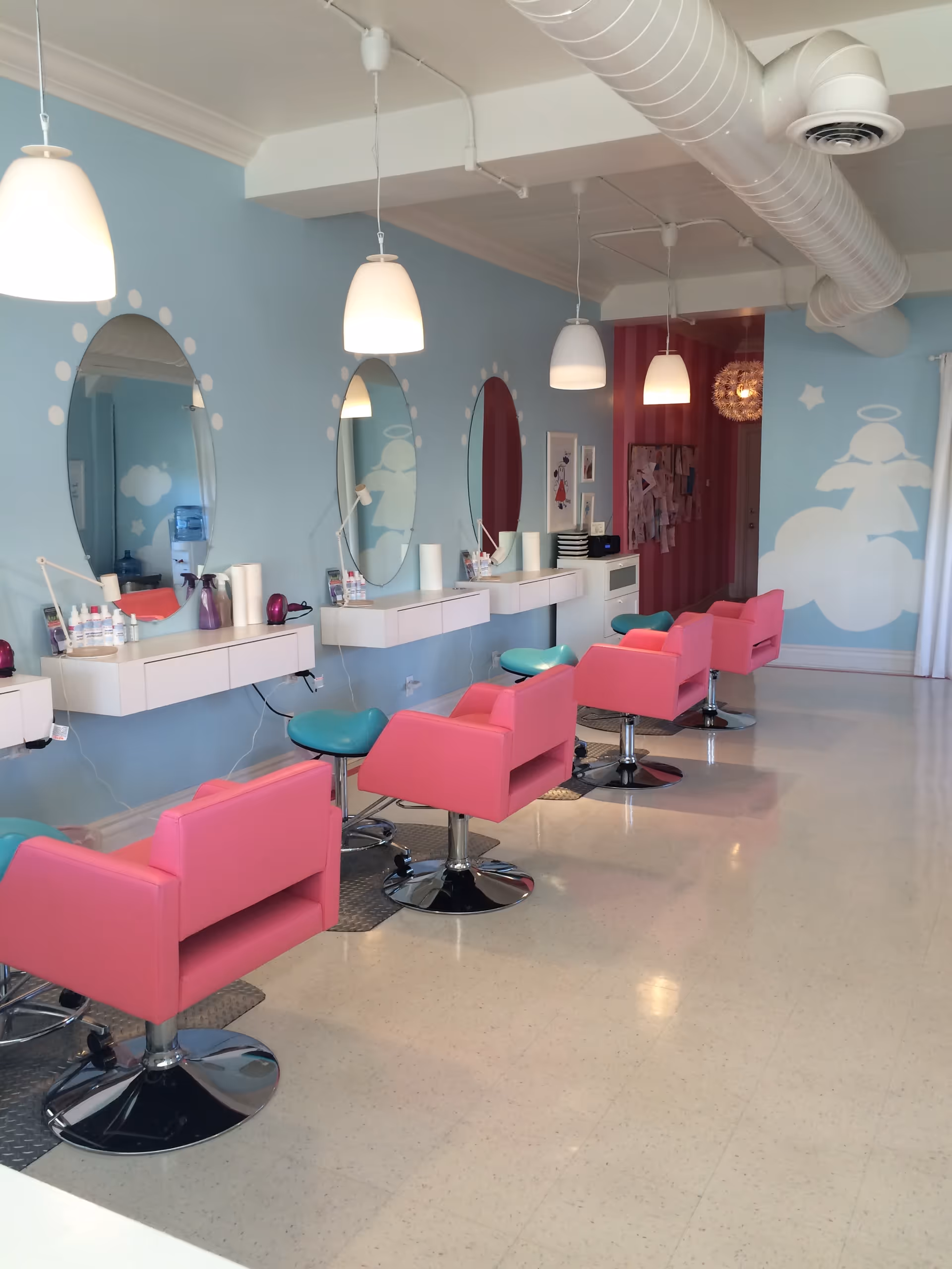 A pastel-themed senior living salon with pink chairs, round mirrors, and bright pendant lights.