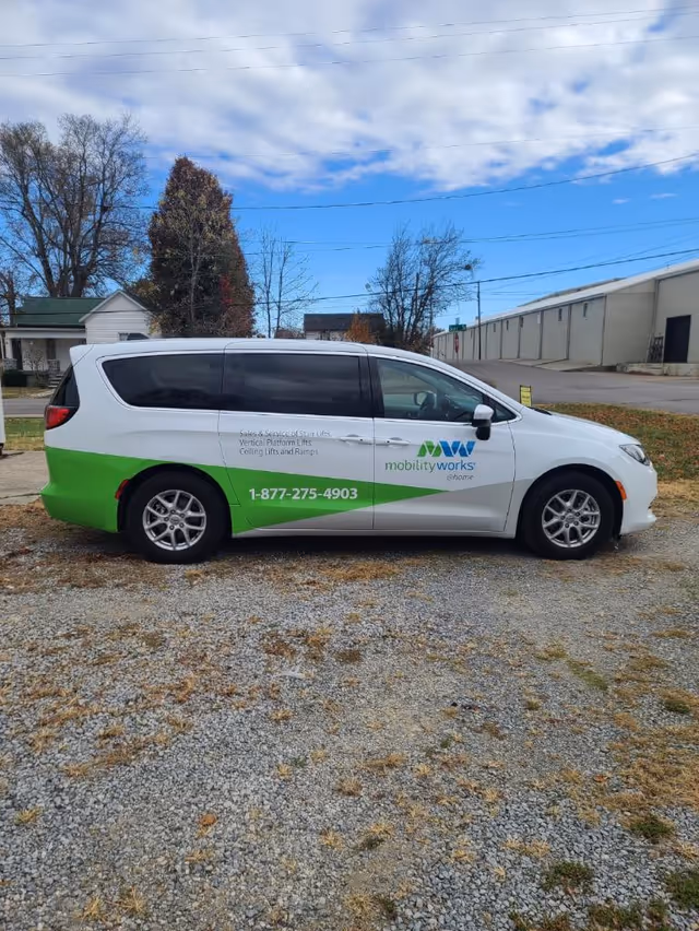 White MobilityWorks van with green accents parked on gravel lot beside a facility.