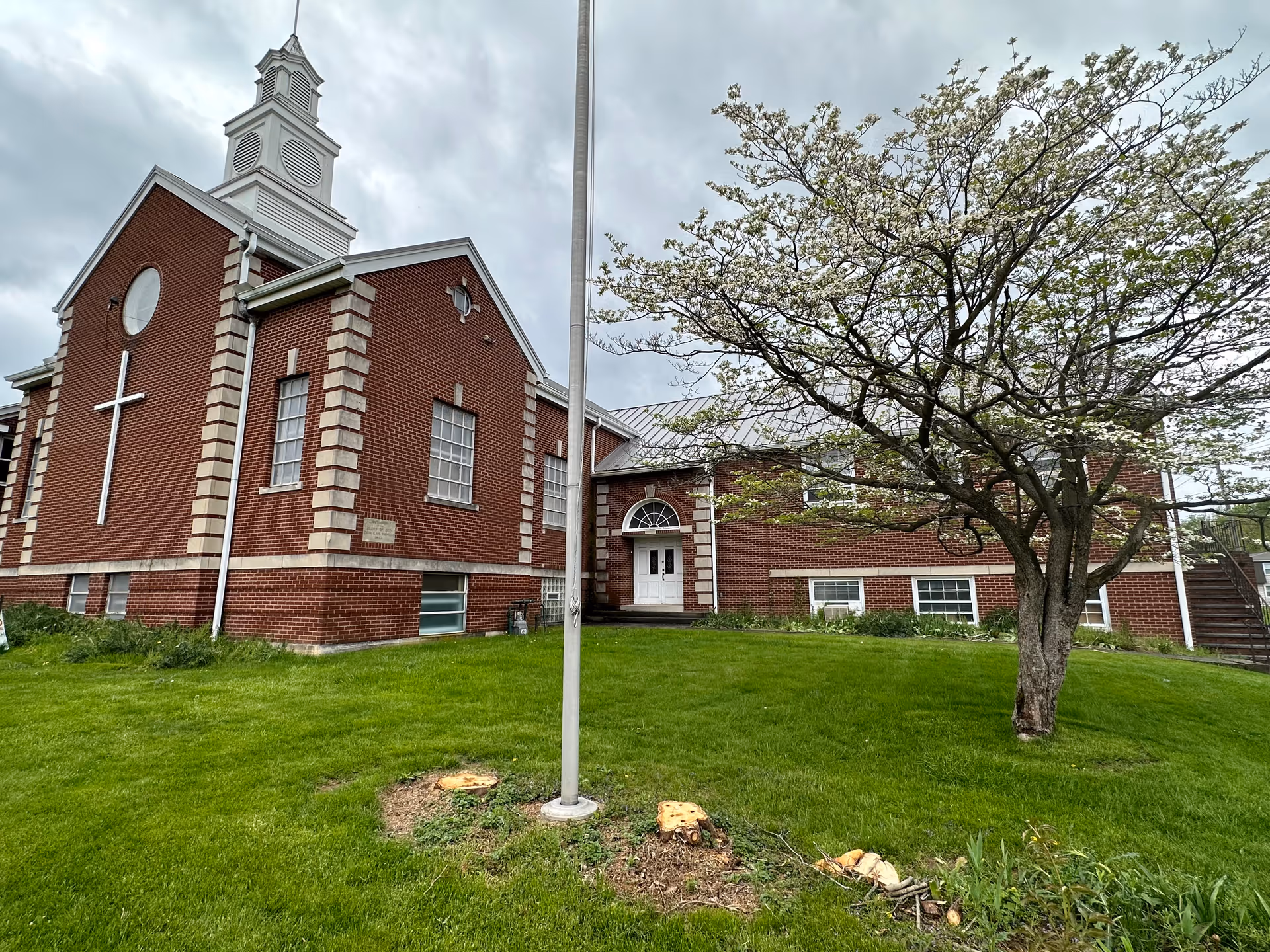 Red brick church-style facility with cross, white trim, and surrounding green lawn.
