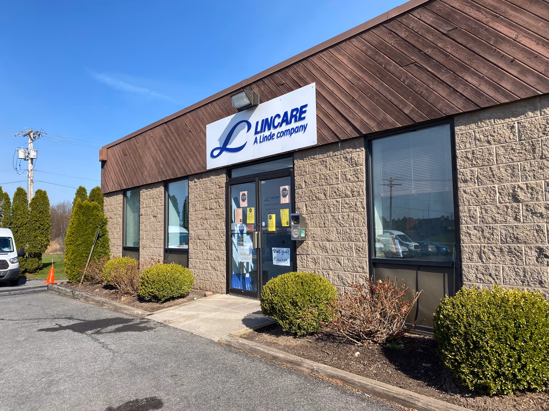 Exterior view of LINCARE building with sign, entrance door, and trimmed shrubs.