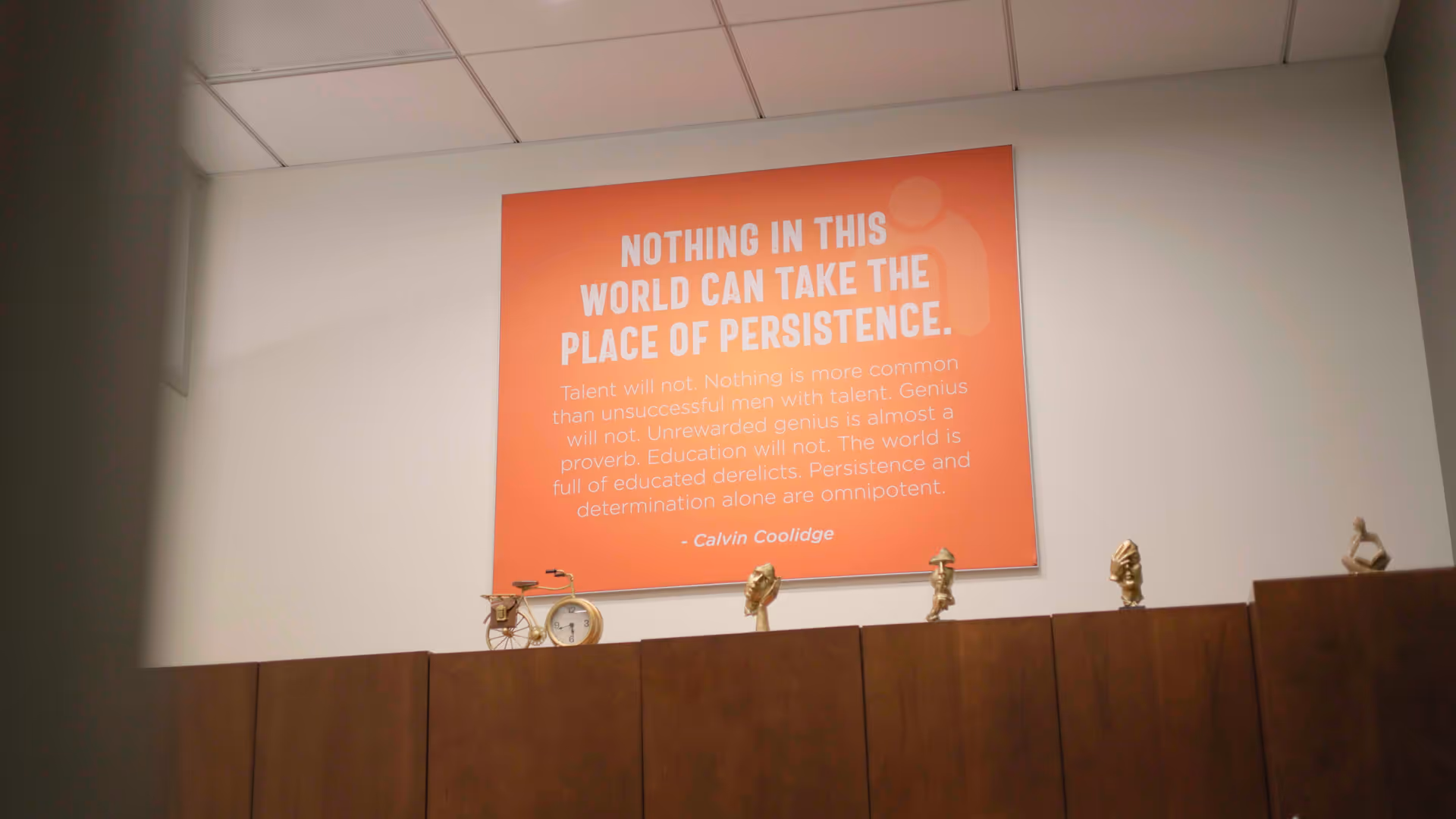 An orange poster on a white wall above dark cabinets with small sculptures.