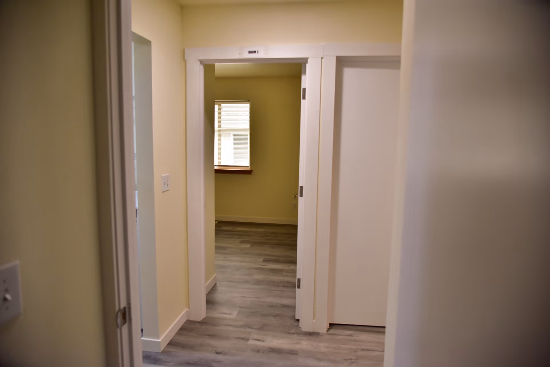 Interior hallway in a senior living facility with pale yellow walls and doorways.