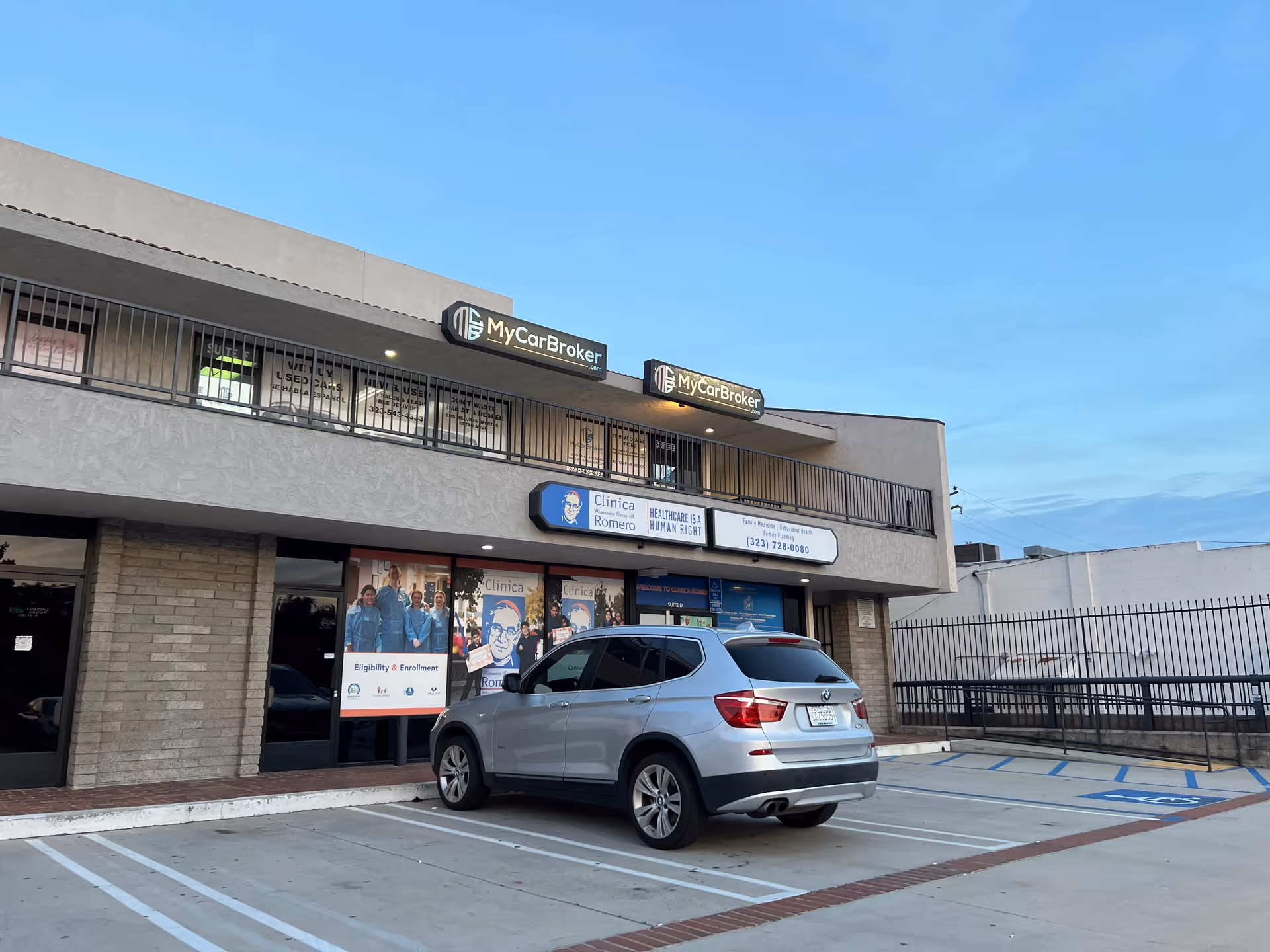 Clinica Monsenor Oscar A. Romero storefront with parked SUV and clear blue sky.
