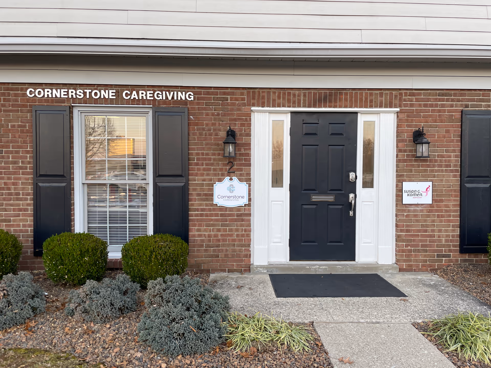 Brick building front with black door, window, shrubs, and Cornerstone Caregiving sign.