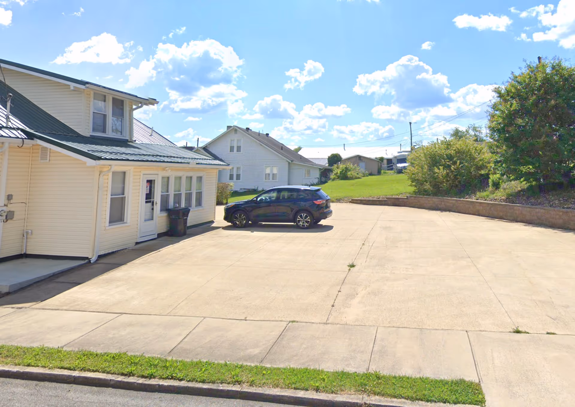 A light-colored senior living facility exterior with a driveway and parked car.