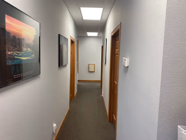A well-lit indoor corridor with framed artwork and wooden doors along a carpeted hallway.