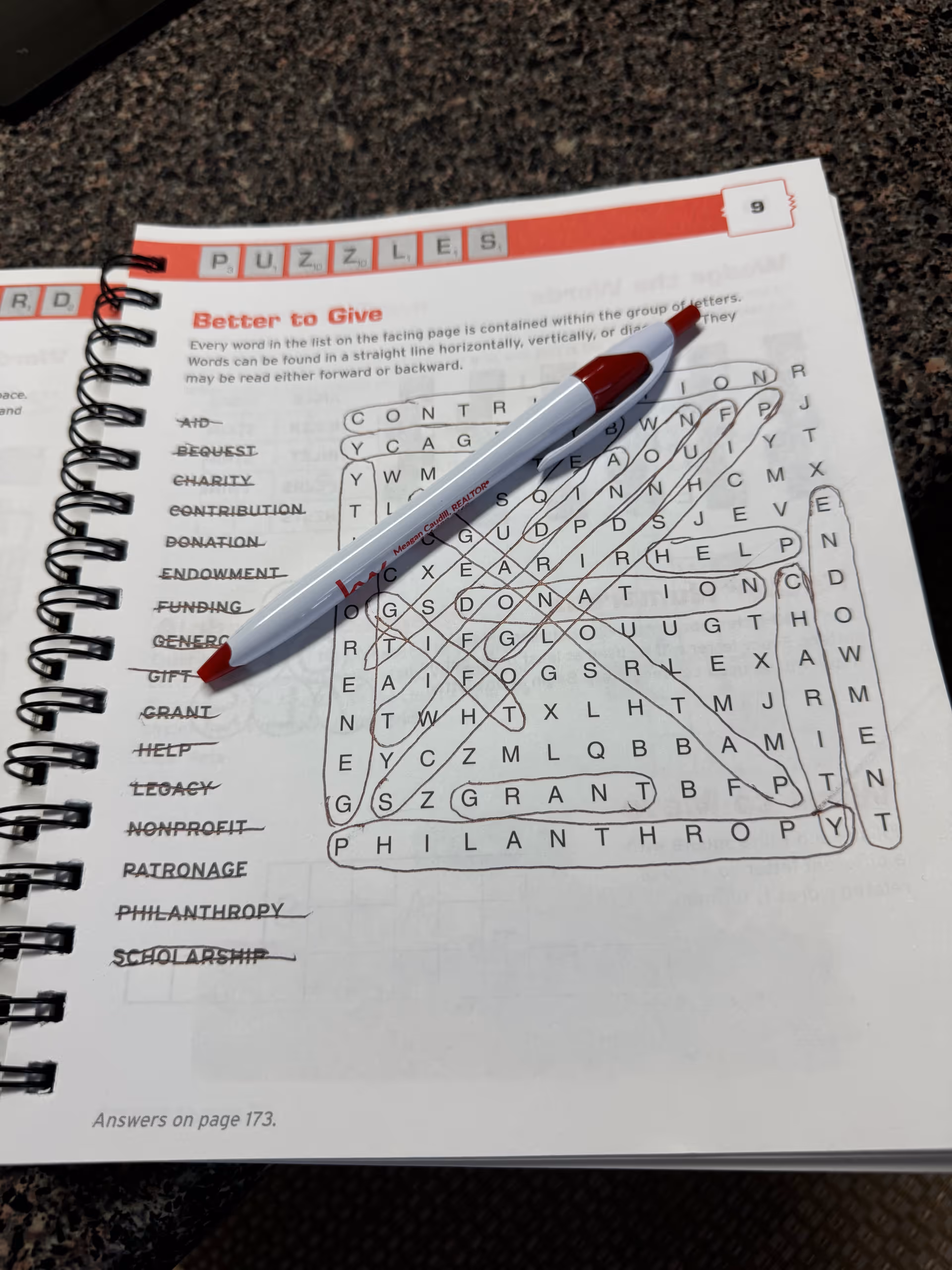 Spiral notebook page with a word search puzzle and red pen on a desk.