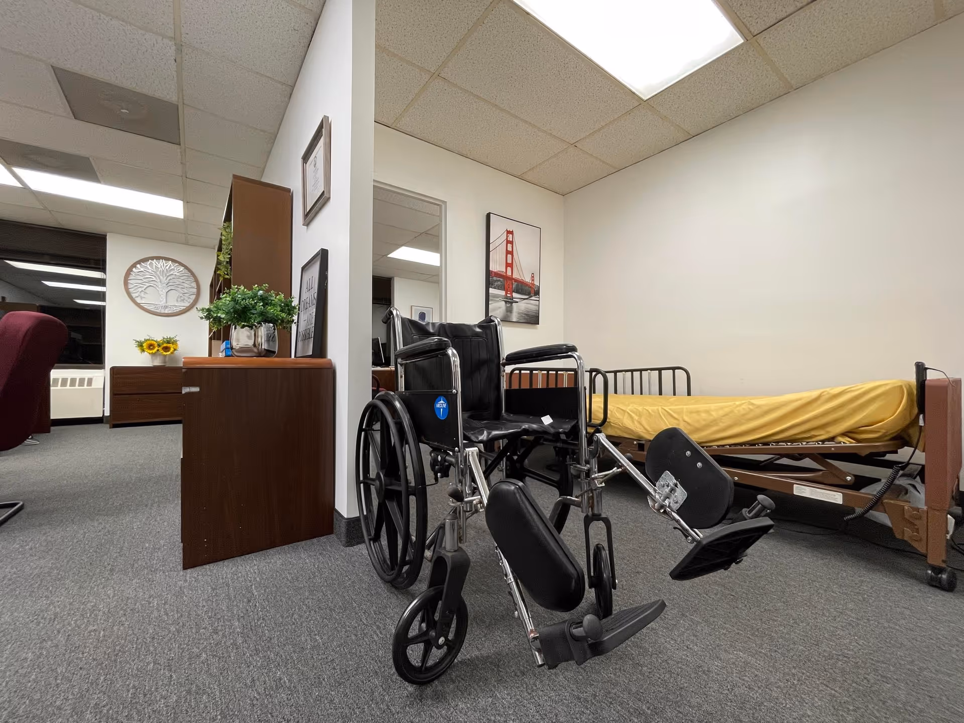 Wheelchair, hospital bed, and furniture in an interior care room.