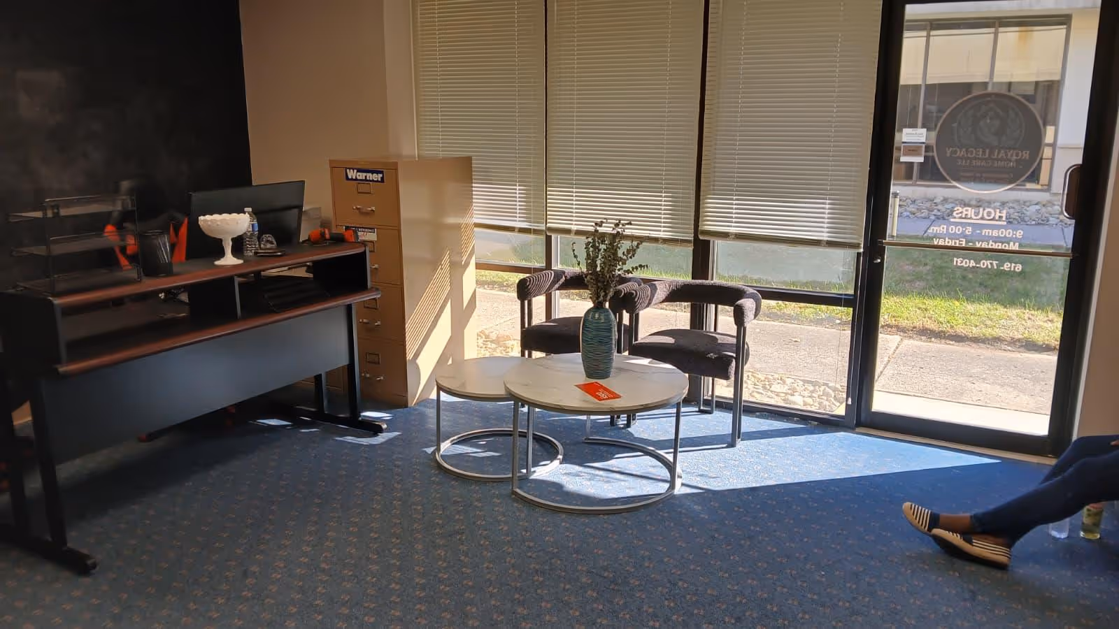 Office lobby with desk, filing cabinet, round coffee table, and chairs by windows.