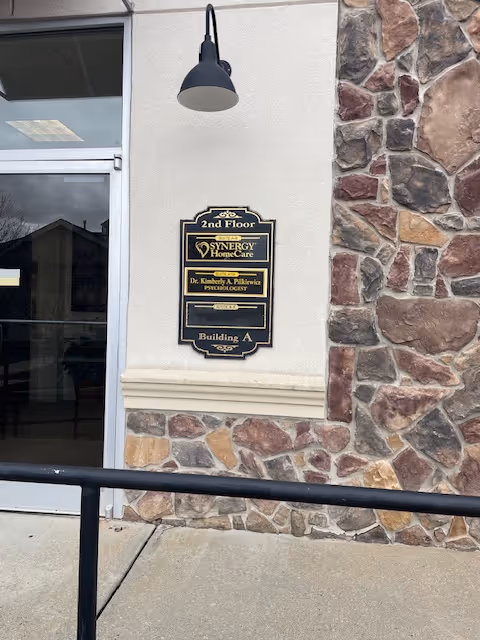 Exterior wall of a Synergy HomeCare facility with a sign and stone facade.