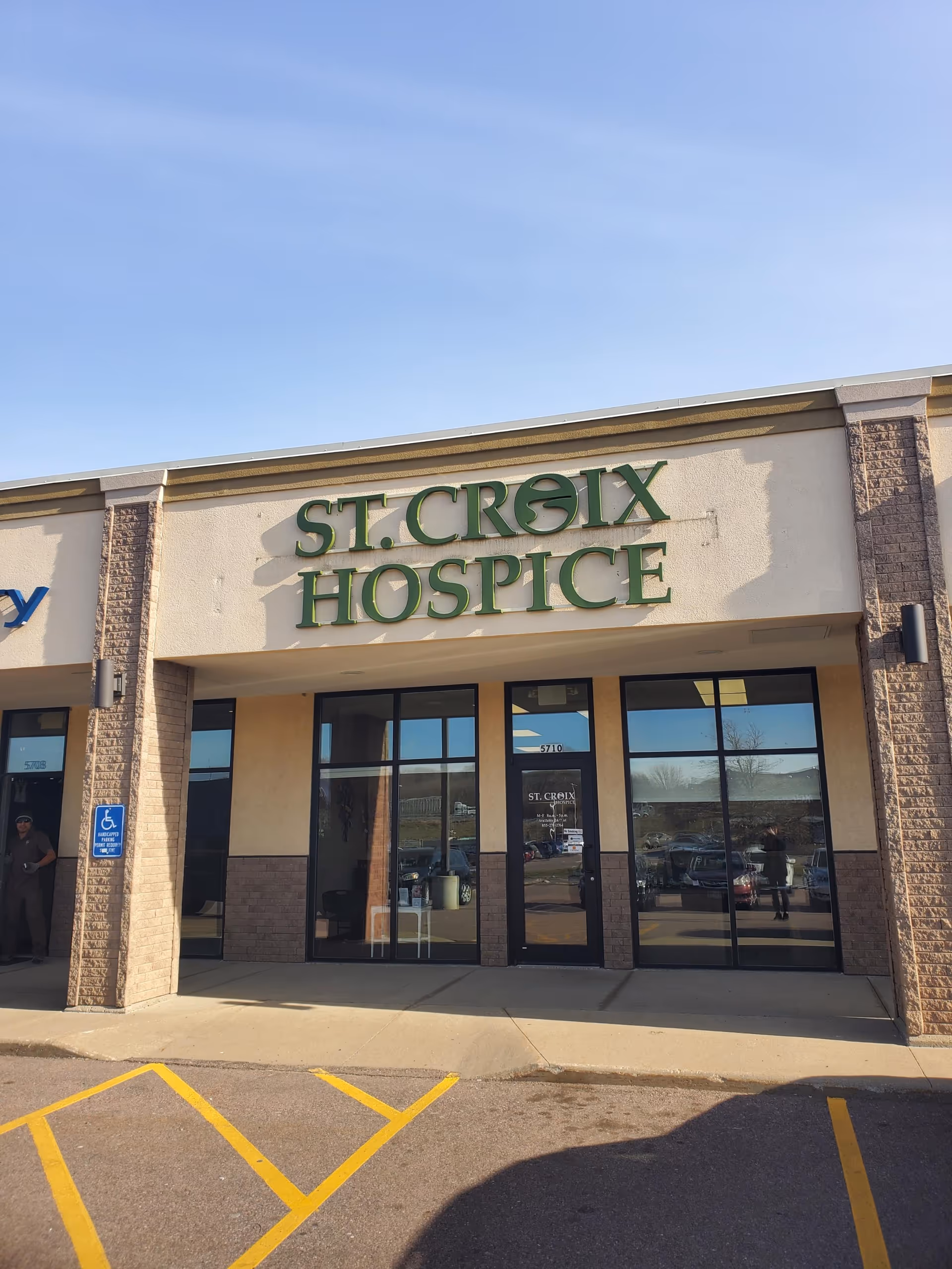 Front exterior of St. Croix Hospice with a large green sign and glass entrance doors.