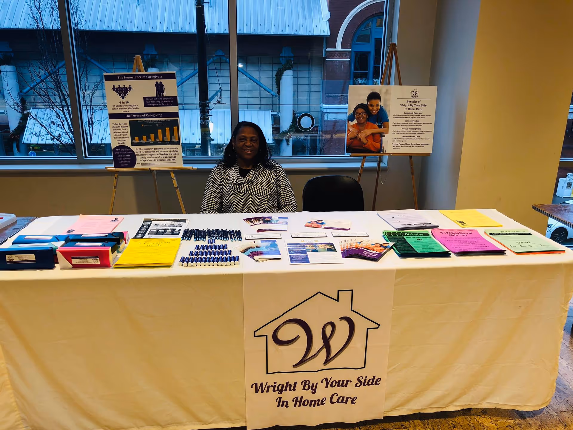 A staff member sits behind a table for Wright By Your Side In Home Care indoors.