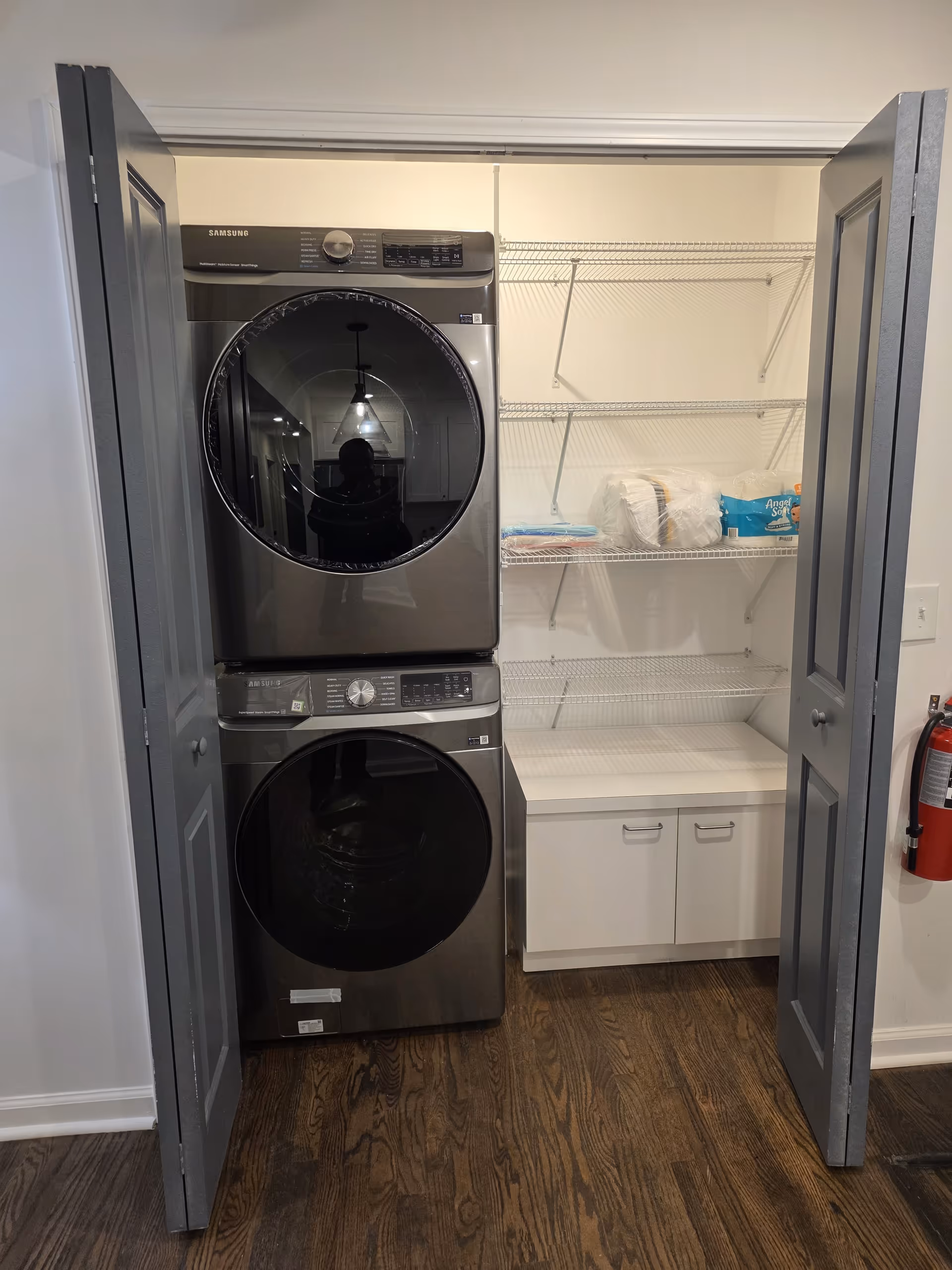 Stacked washer and dryer in a closet with wire shelving and a small cabinet